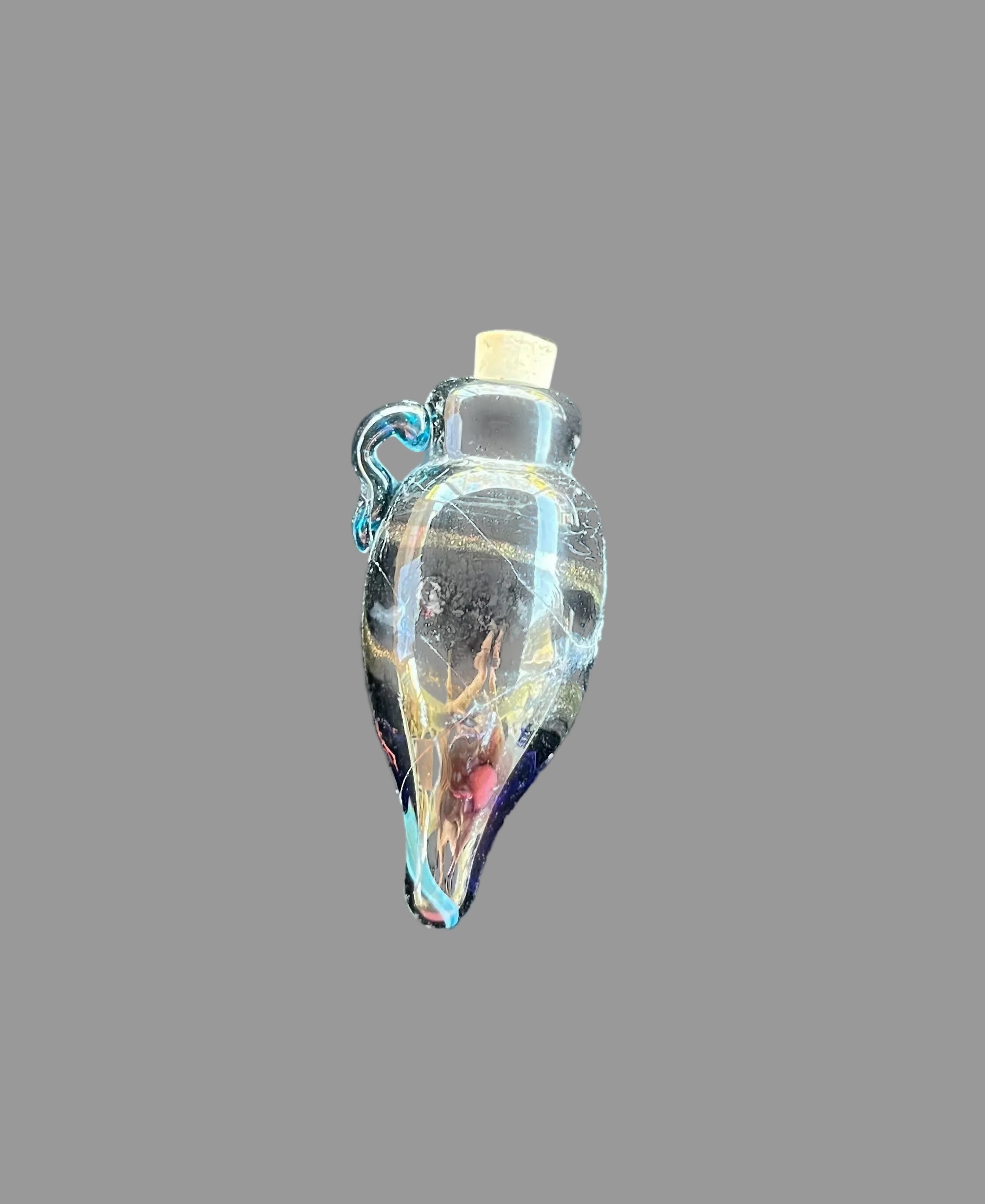 A small hand-blown glass bottle pendant with a cork stopper, featuring swirls of blue, gold, and red glass, resting on a dark textured surface.
