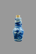 A small glass bottle with a cork stopper, featuring a marbled swirl pattern of blue, white, and gray, set against a dark textured background.