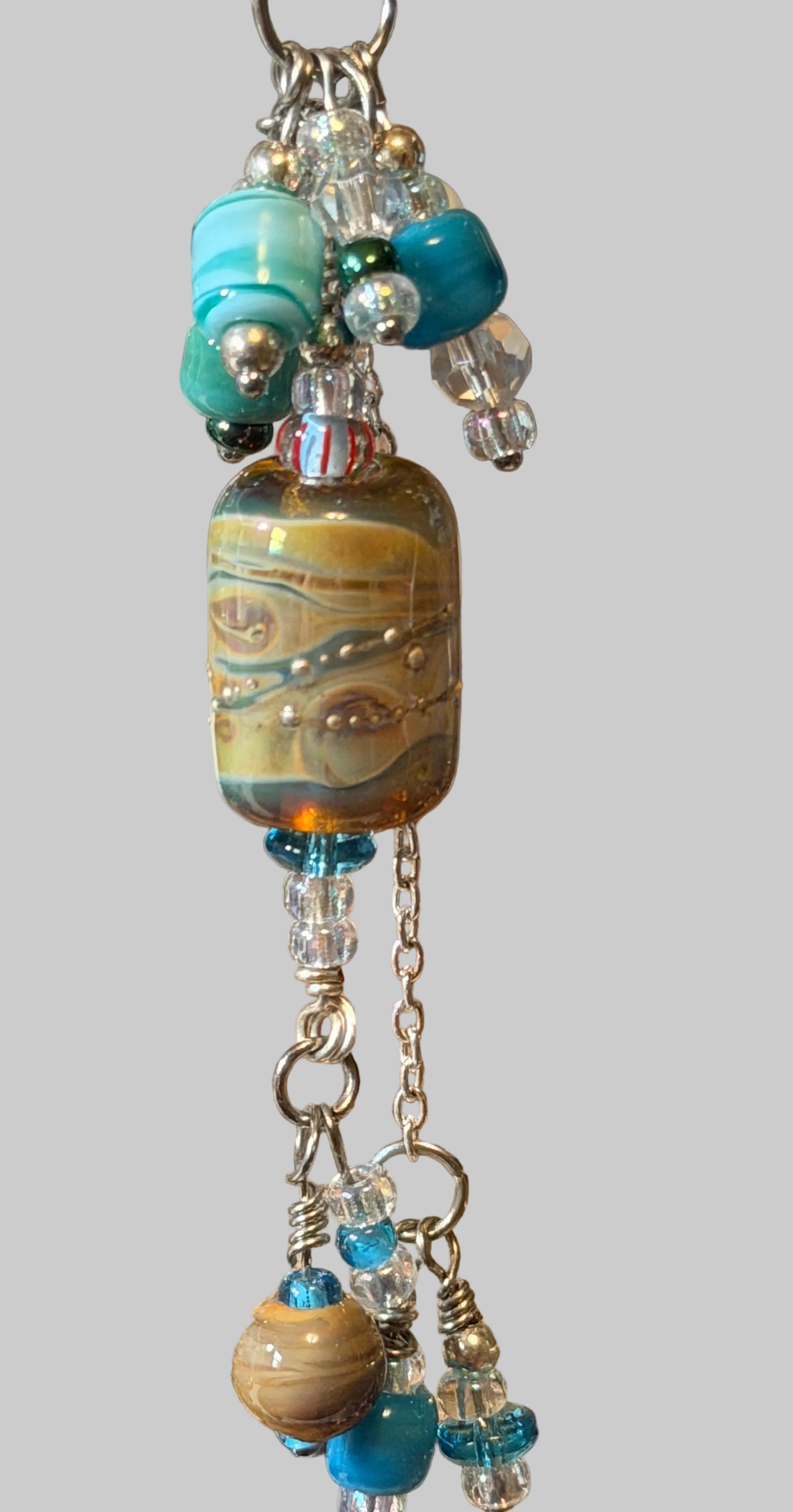 A close-up of a handmade beaded keychain or keyring charm with a large marbled lampwork bead, turquoise and blue beads, clear glass beads, and silver-toned chains.