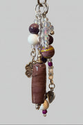 A beaded keychain or bag charm with a long purple stone, white beads, purple beads, clear faceted beads, and silver-toned metal charms.