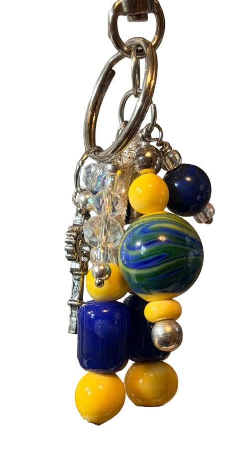 A close-up of a beaded keychain with yellow, navy blue, and green marbled beads, silver-toned metal rings, and clear crystal charms.