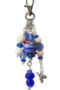 A blue and white beaded bag charm with a marbled glass bead, white beads, blue glass beads, silver metal rings, and a dangling silver bird charm.