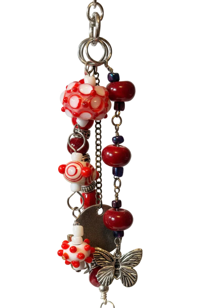 A handmade beaded keychain or charm with red and white patterned glass beads, dark red beads, silver-tone metal rings, and a butterfly charm. 