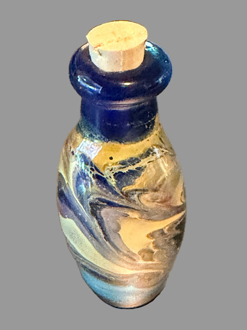 A small decorative glass bottle with a cork stopper, featuring a cobalt blue neck and a marbled body of cream, white, and blue glass.