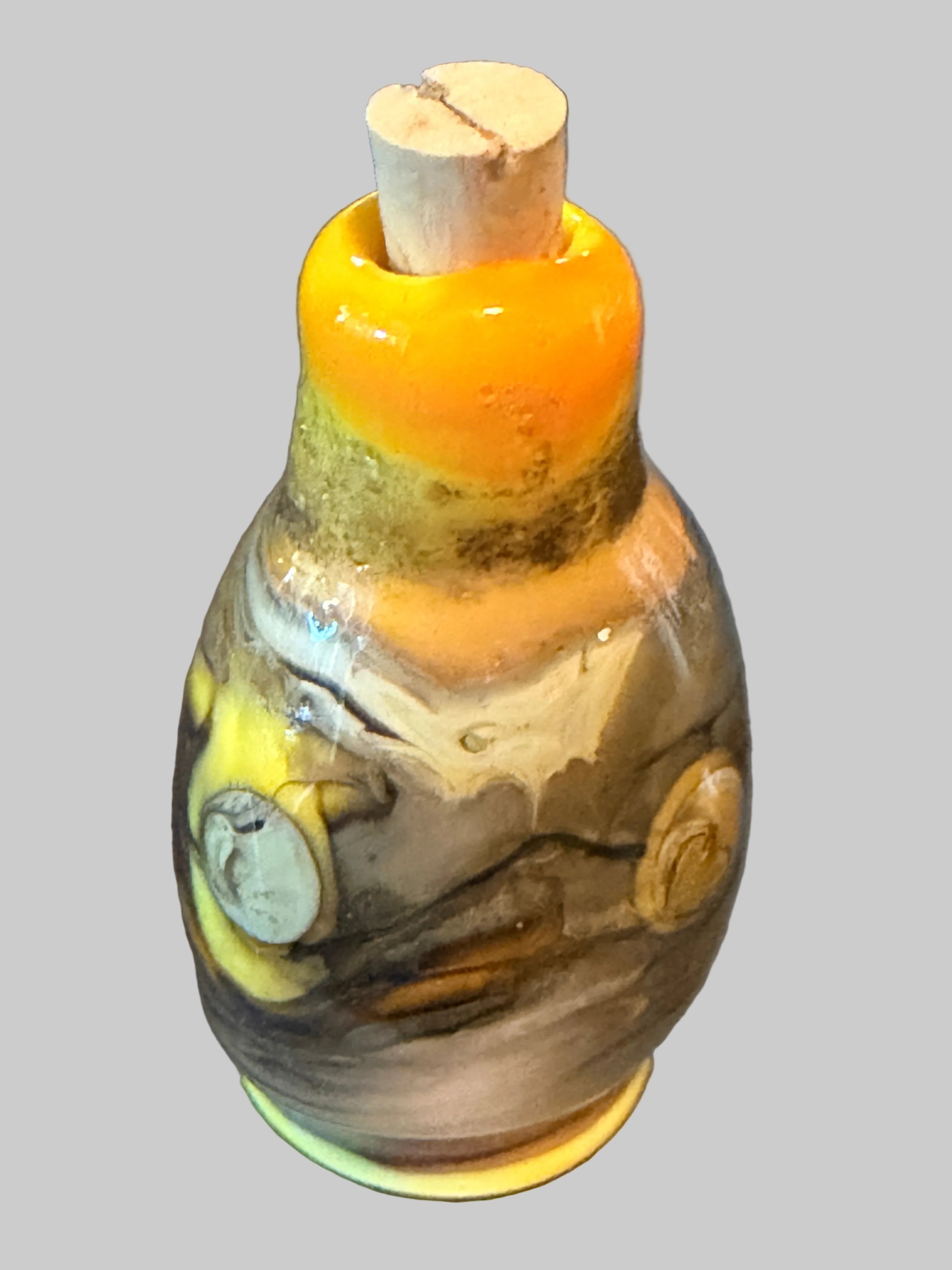 A handcrafted glass bottle with a cork stopper, featuring a marbled pattern of brown, gray, yellow, and white glass with a vibrant orange-yellow section at the neck.
