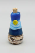 A small handcrafted glass bottle with a cork stopper, featuring a sunny summer day at the lake.