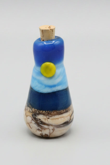 A small handcrafted glass bottle with a cork stopper, featuring a sunny summer day at the lake.