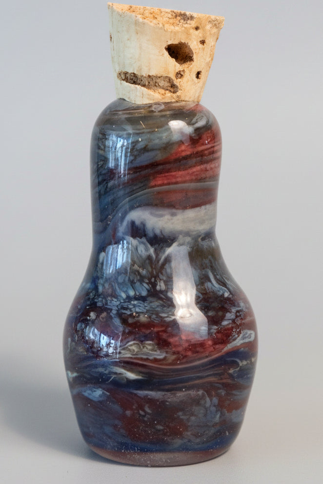 A small decorative bottle with a cork stopper, featuring a marbled pattern of brown, gray, and red glass. 